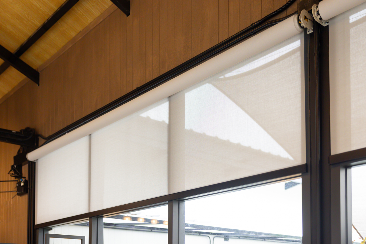 A white blind is hanging from a window. The blind is made of a white material and is hanging from a black rod